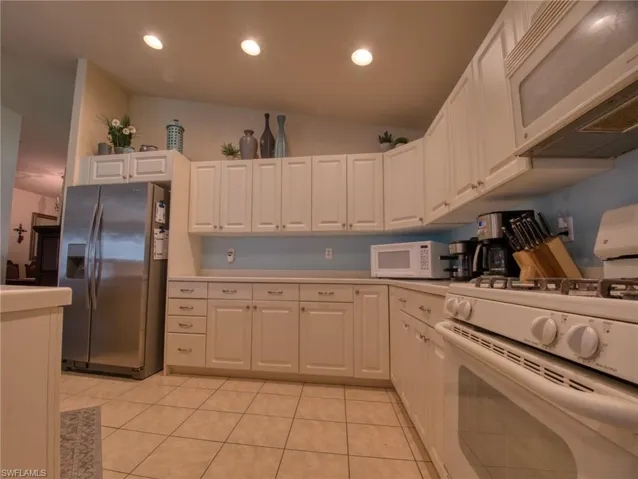 Kitchen with white appliances, white cabinets, light countertops, recessed lighting, and vaulted ceiling