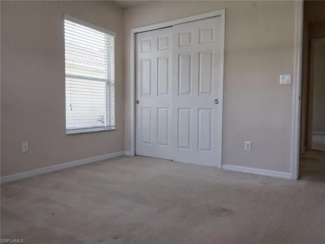 Bedroom featuring neutral-toned carpeting, a window with horizontal blinds, and a closet with white bi-fold doors