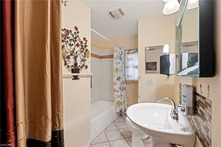 Bathroom featuring tile patterned flooring, shower / bath combination with curtain, and sink