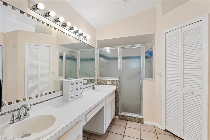 Bathroom featuring tile patterned floors, vanity, lofted ceiling, and a shower with door