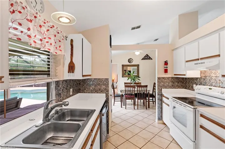 Kitchen featuring dishwasher, sink, white electric stove, light tile patterned floors, and white cabinetry