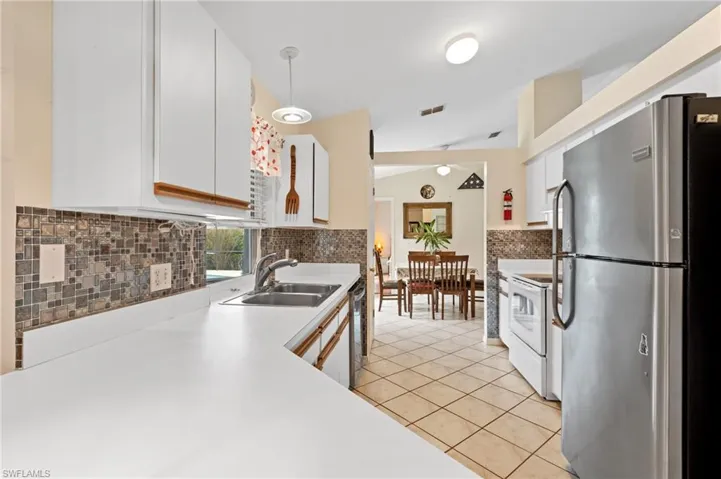 Kitchen with sink, decorative backsplash, light tile patterned floors, white cabinetry, and stainless steel appliances