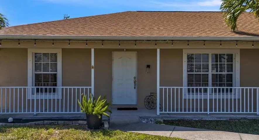View of exterior entry featuring roof with shingles, stucco siding, and a porch