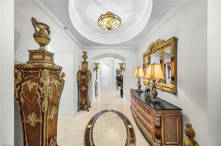 Hall with inlaid floor details, arched walkways, a tray ceiling, and crown molding