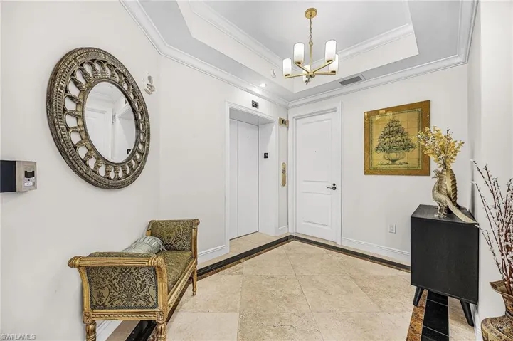 Foyer entrance featuring inlaid floor details, a raised ceiling, elevator, a chandelier, and ornamental molding