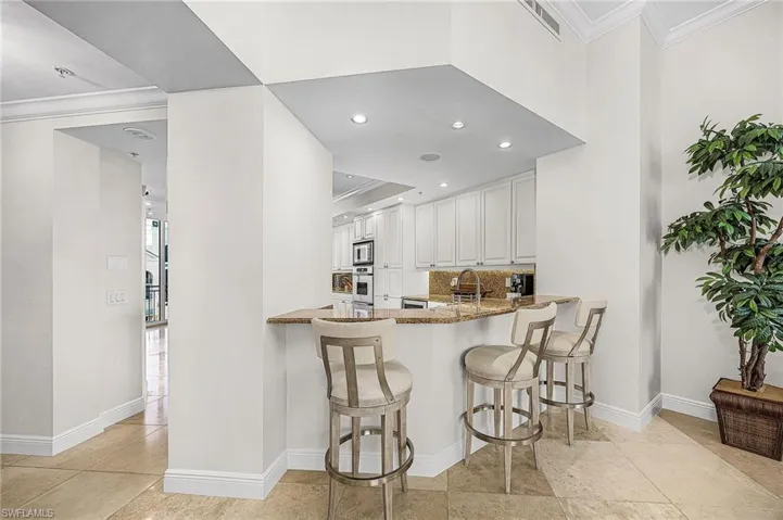 Kitchen with crown molding, a breakfast bar area, white cabinets, light stone counters, and a peninsula