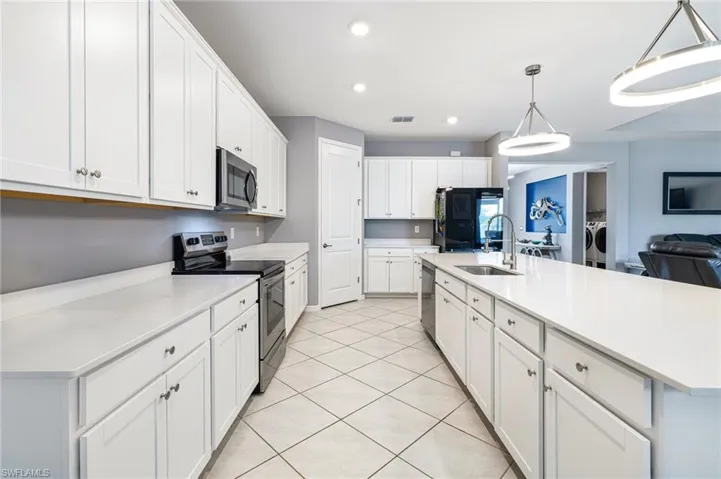 Spacious kitchen featuring white cabinetry, light countertops, stainless steel appliances, a large island with sink, and overhead pendant lighting