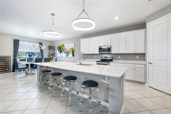Expansive kitchen island with seating, white shaker cabinetry, stainless steel appliances, and tile flooring