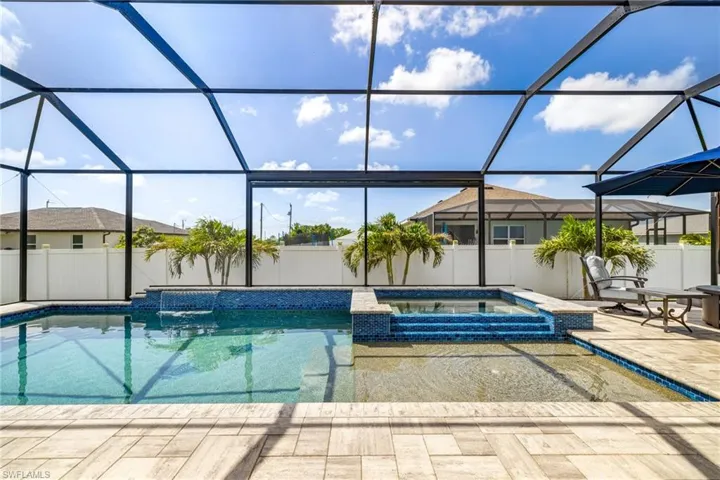 Screened outdoor living space featuring a swimming pool with an integrated spa, mosaic tile accents, and a waterfall feature