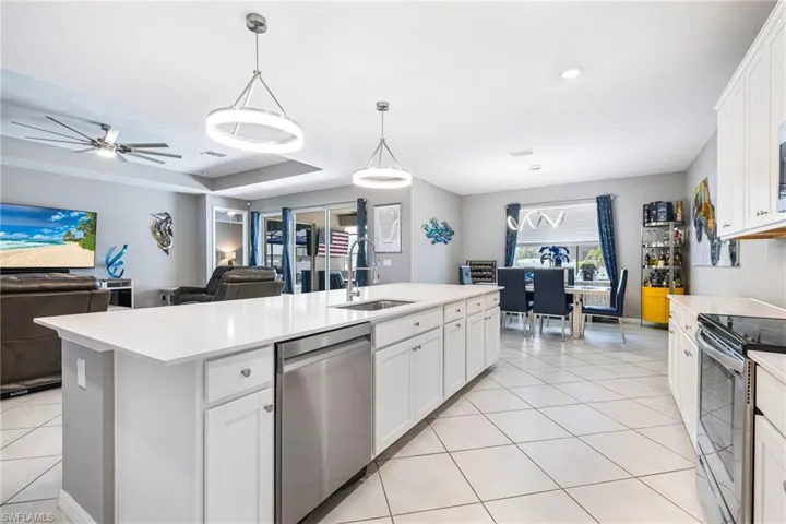 Spacious open-concept kitchen featuring a large central island with a sink and stainless steel dishwasher, white cabinetry, and light-toned countertops