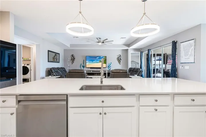 Expansive kitchen island featuring a stainless steel undermount sink, integrated dishwasher, and white shaker-style cabinetry with circular hardware