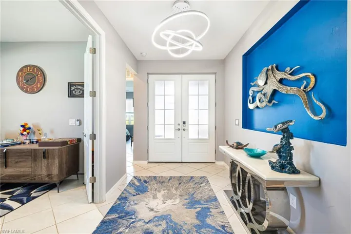 Entryway featuring double French doors with frosted glass panels, a contemporary overhead light fixture, light-toned tile flooring, and a recessed wall accent