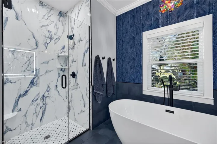 Full bathroom with a freestanding tub, tile walls, a marble finish shower, wainscoting, and crown molding