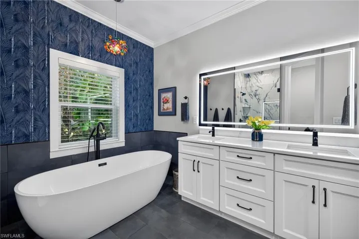 Full bath with a marble finish shower, wainscoting, a soaking tub, wallpapered walls, and double vanity