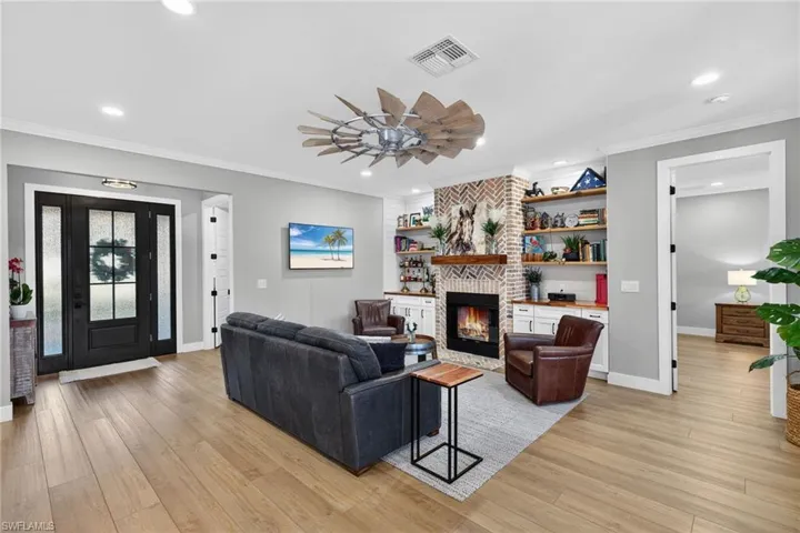 Living room with a fireplace, a ceiling fan, light wood-style flooring, recessed lighting, and crown molding