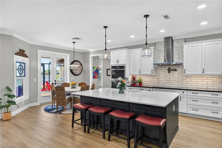 Kitchen featuring tasteful backsplash, wall chimney range hood, white cabinets, crown molding, and recessed lighting