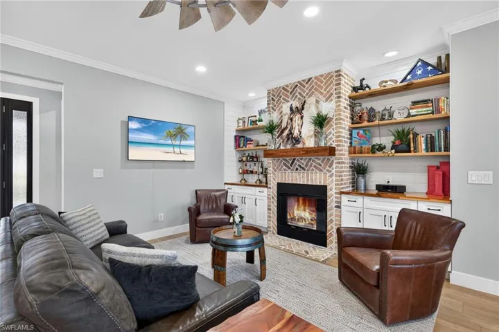 Living room featuring a fireplace, light wood-style floors, a ceiling fan, ornamental molding, and recessed lighting