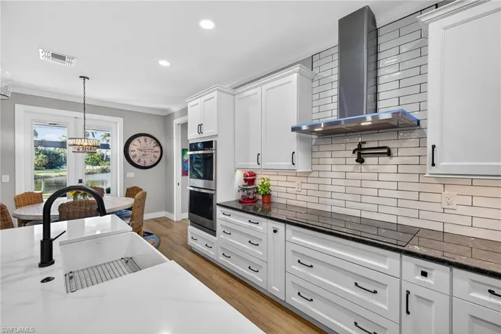 Kitchen with wall chimney range hood, ornamental molding, pendant lighting, white cabinetry, and dark stone countertops