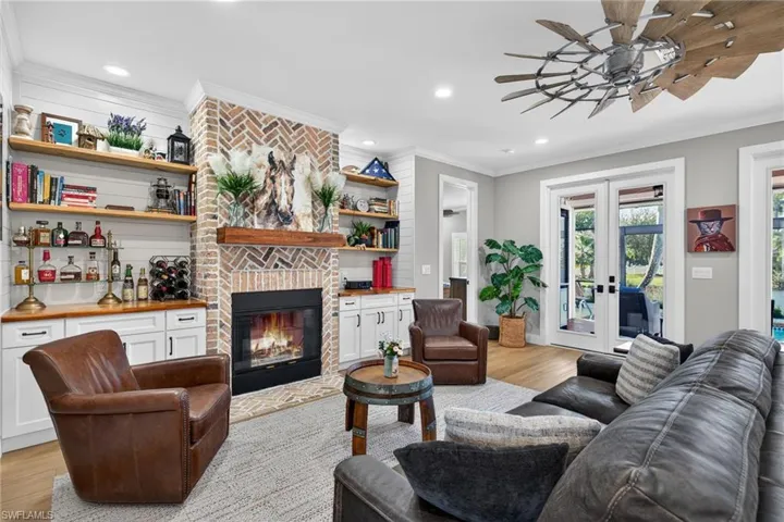 Living area with french doors, light wood-style floors, crown molding, a brick fireplace, and recessed lighting