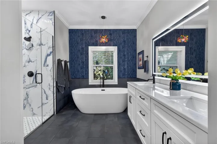 Full bath with a marble finish shower, double vanity, tile walls, a freestanding bath, and ornamental molding
