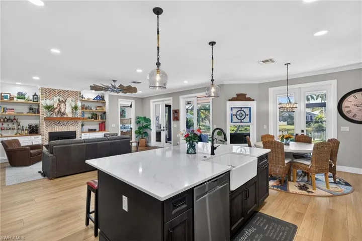 Kitchen featuring dark cabinetry, open floor plan, light wood-type flooring, stainless steel dishwasher, and pendant lighting
