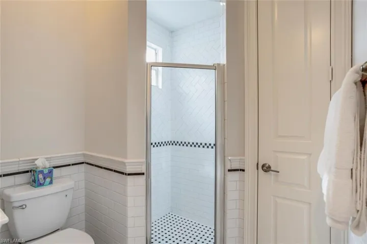 Bathroom with a shower with door, tile walls, and toilet