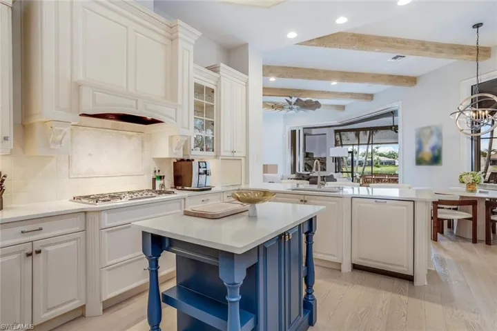 Kitchen with a breakfast bar, beamed ceiling, light hardwood / wood-style floors, a kitchen island, and stainless steel gas stovetop