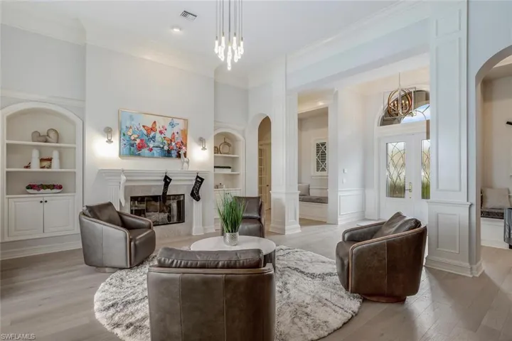 Sitting room with built in shelves, an inviting chandelier, a high end fireplace, crown molding, and light hardwood / wood-style floors