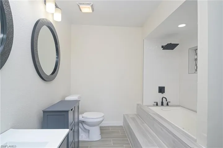 Bathroom featuring vanity, wood finish floors,  shower combination, and recessed lighting