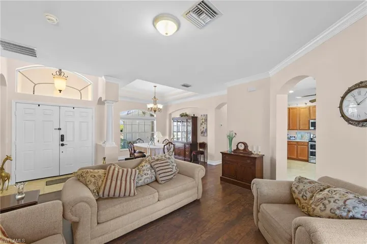Living area featuring arched walkways, crown molding, dark wood finished floors, and hanging lights