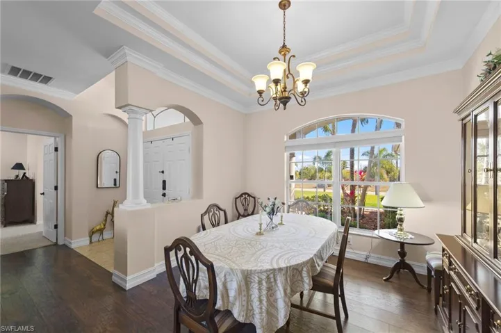 Dining room with a raised ceiling, wood-type flooring, ornamental molding, arched walkways, and hanging lights