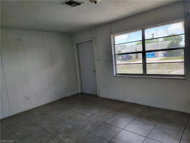 Room featuring square-tiled flooring, a paneled accent wall, a window with horizontal muntins, a white door, and a ceiling vent