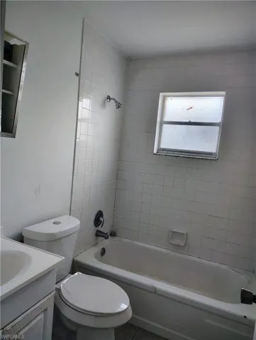 Bathroom featuring a built-in bathtub with white tile surround, a single-pane window, and a vanity with an integrated sink