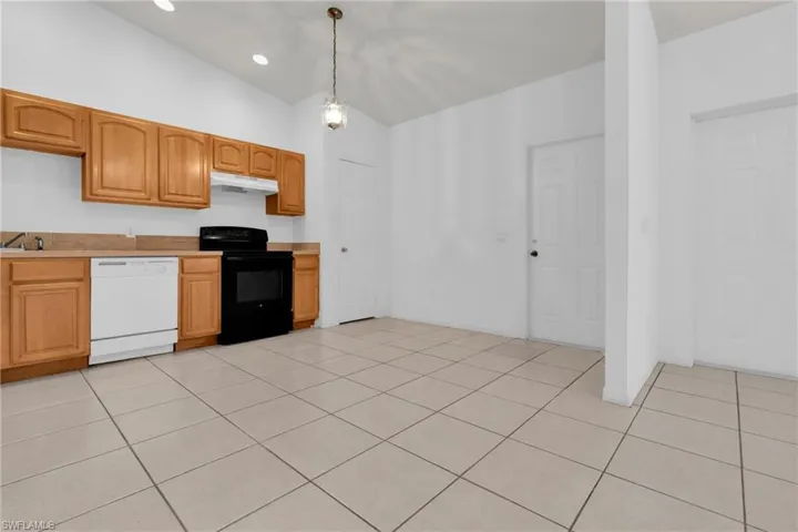 Kitchen featuring black range with electric cooktop, white dishwasher, lofted ceiling, light countertops, and light tile patterned floors