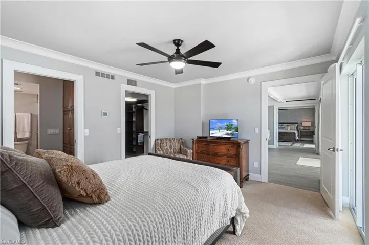Bedroom with crown molding, a walk in closet, carpet, connected bathroom, and ceiling fan