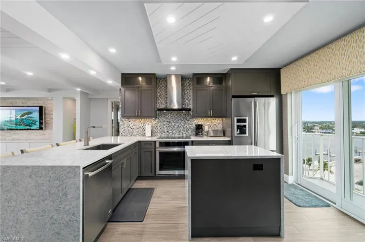 Kitchen featuring light stone counters, backsplash, appliances with stainless steel finishes, a peninsula, and a kitchen island