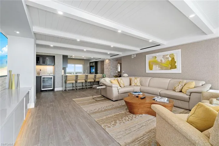 Living room with beam ceiling, beverage cooler, wood finished floors, bar with sink, and recessed lighting