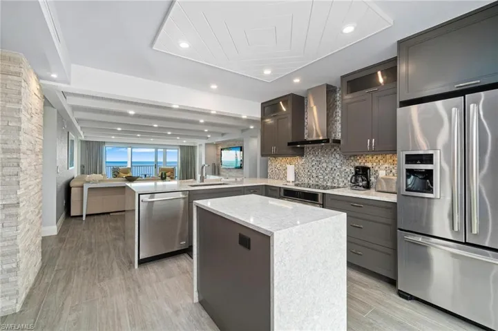 Kitchen featuring appliances with stainless steel finishes, a peninsula, open floor plan, light stone countertops, and glass insert cabinets