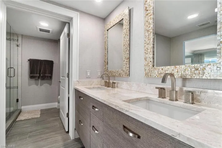 Full bathroom featuring double vanity, a shower stall, recessed lighting, and light wood-type flooring