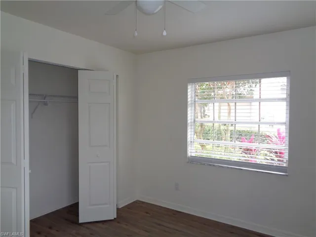Unfurnished bedroom with a closet, dark wood-style floors, and a ceiling fan