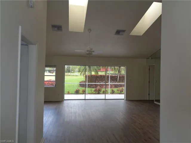 Unfurnished room with dark wood-style floors, ceiling fan, lofted ceiling, and a skylight