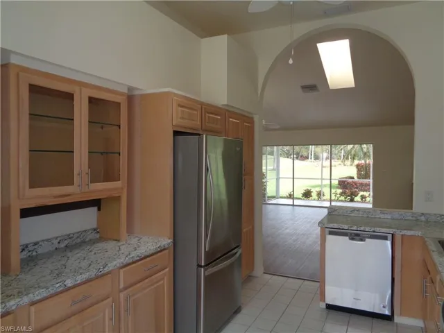 Kitchen featuring stainless steel appliances, glass insert cabinets, light tile patterned flooring, arched walkways, and a skylight