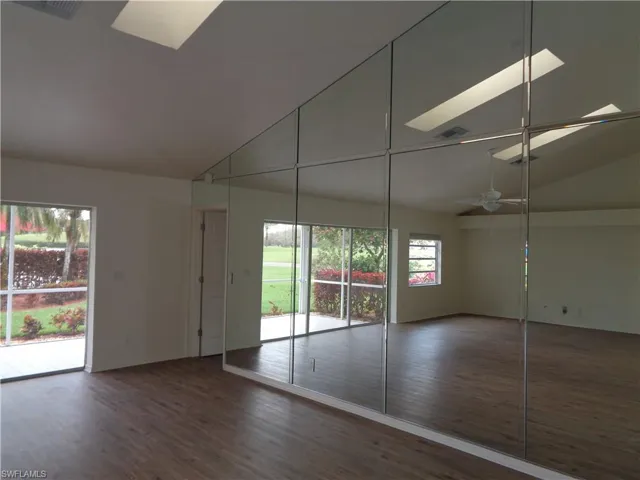 Unfurnished bedroom featuring access to exterior, a skylight, dark wood-type flooring, and high vaulted ceiling