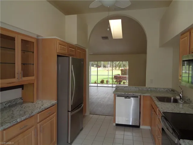 Kitchen with appliances with stainless steel finishes, glass insert cabinets, arched walkways, and light stone counters