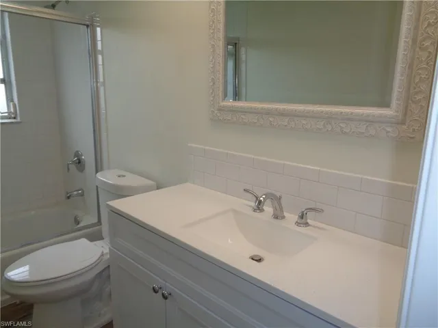 Bathroom featuring enclosed tub / shower combo, vanity, and tasteful backsplash
