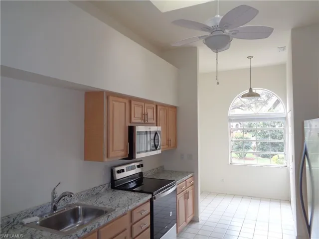 Kitchen featuring stainless steel appliances, light stone counters, light brown cabinets, and hanging light fixtures