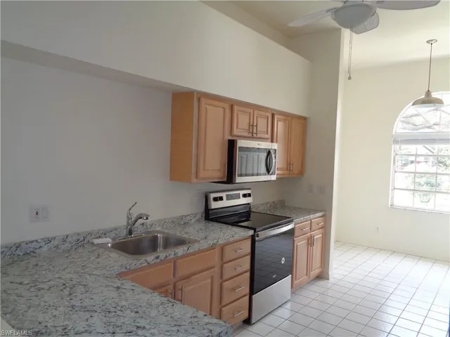 Kitchen with appliances with stainless steel finishes, light tile patterned flooring, hanging light fixtures, light stone countertops, and ceiling fan