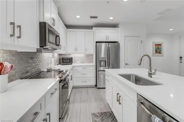 Light, bright kitchen with white cabinetry, stainless steel appliances, decorative backsplash, sink, and under-counter lighting