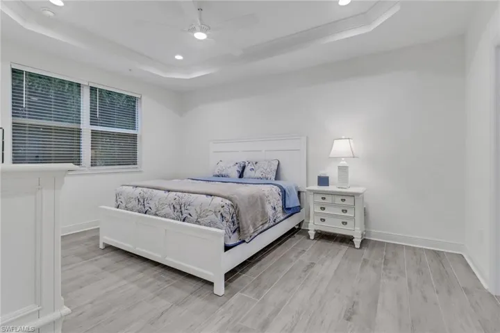 Master bedroom featuring light wood-type flooring, ceiling fan, and a tray ceiling