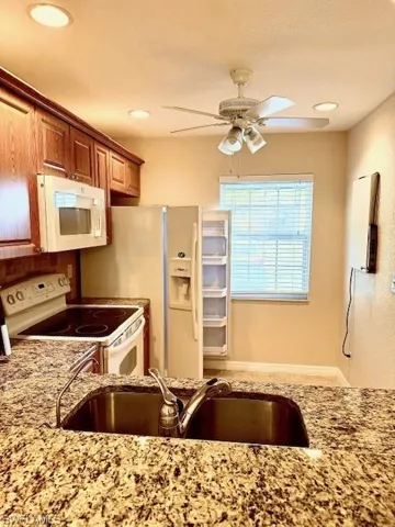 Kitchen featuring ceiling fan, sink, light stone counters, and white appliances